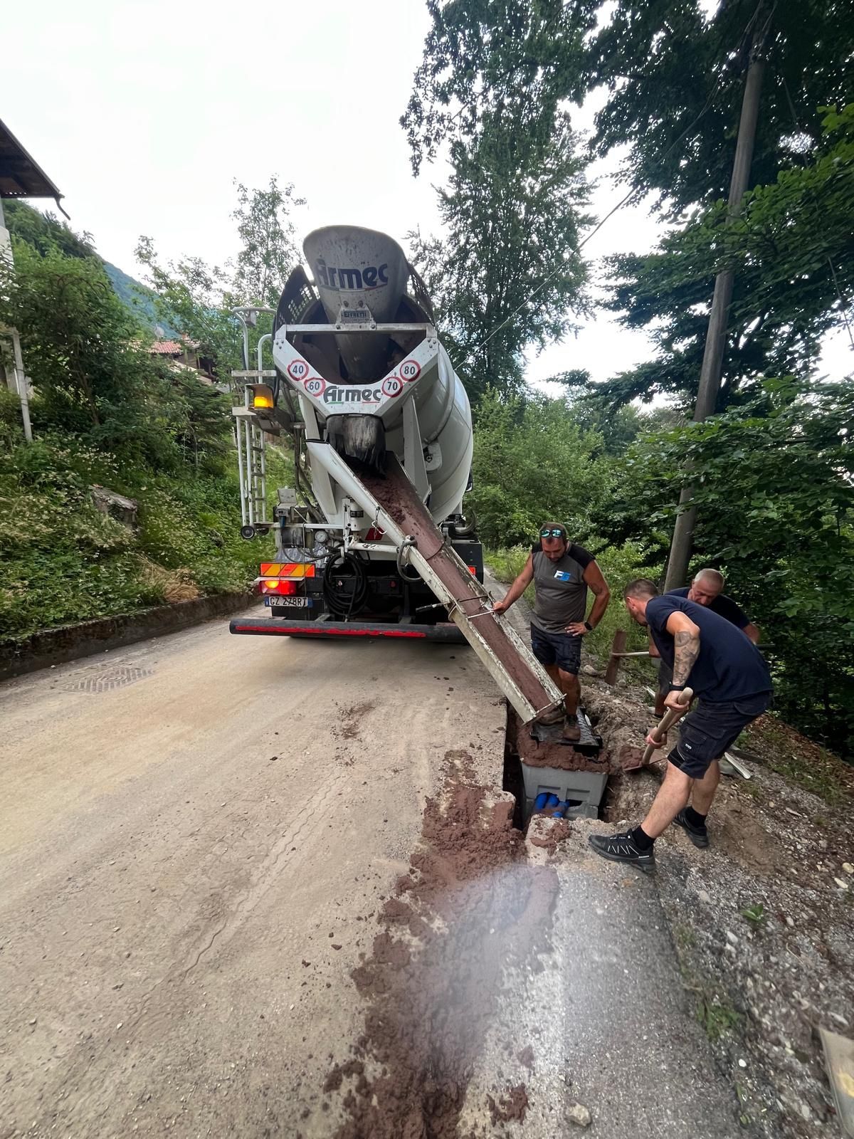 Autobetoniera che scarica calcestruzzo in uno scavo mentre due operatori stendono il getto