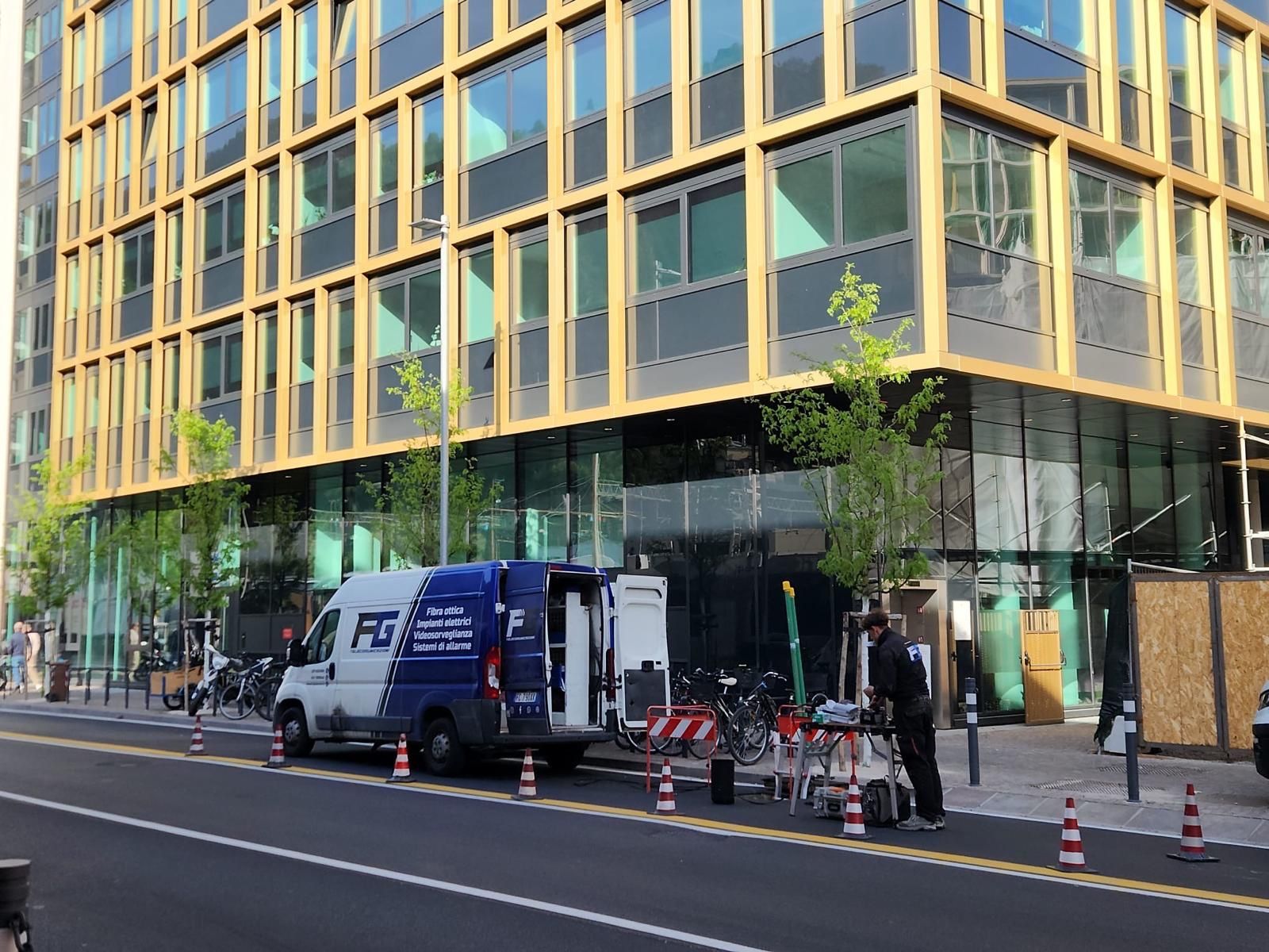 Il furgone di F&G Telecomunicazioni e un tecnico al lavoro in cantiere davanti a un edificio per uffici