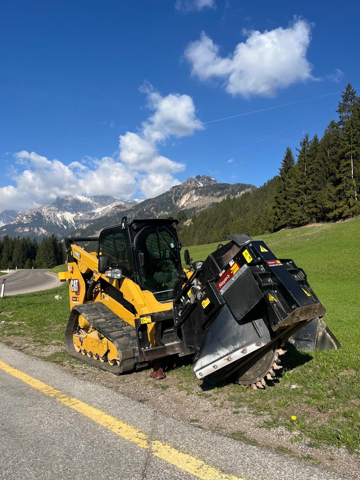 Pala cingolata con fresa a tamburo ferma a bordo strada, con le Dolomiti sullo sfondo
